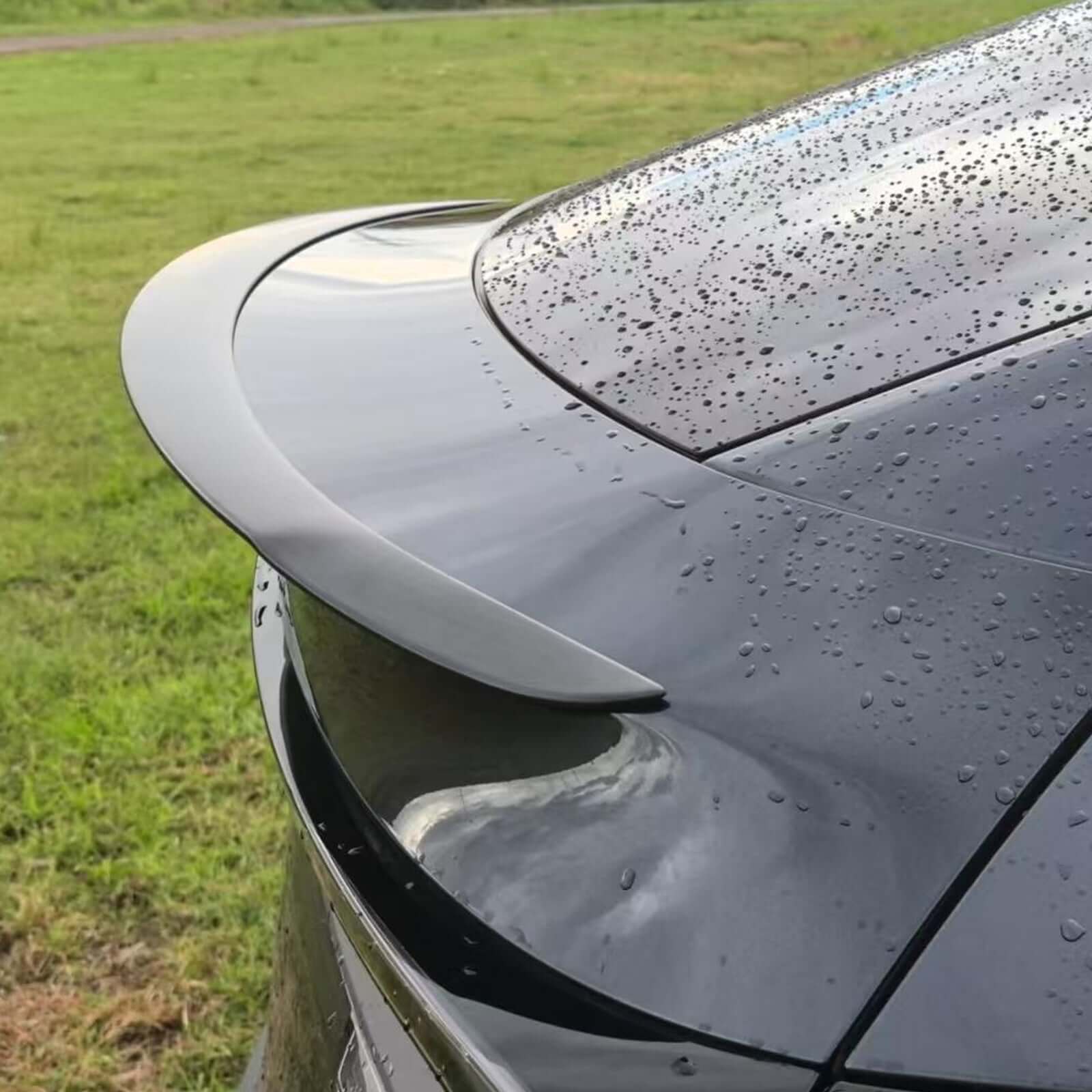 Side view of Real Dry Carbon Spoiler for Tesla Model Y Juniper 2025 showing aerodynamic design with rain droplets